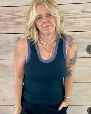 Woman wearing a navy tank top and pants against a wooden background
