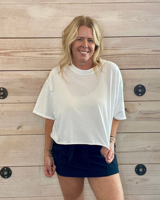 Woman wearing a white t-shirt and black shorts standing against a wooden wall.