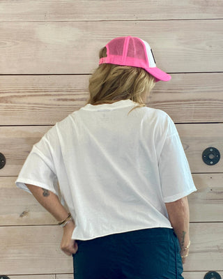 Person wearing a white t-shirt, navy shorts, and pink cap against a wooden wall.