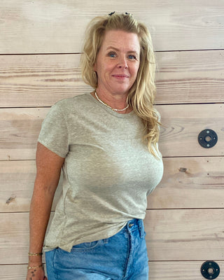 Woman wearing a green t-shirt and blue shorts standing against a wooden wall.