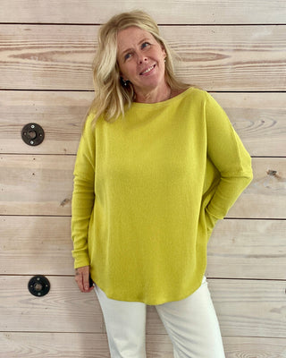 Woman wearing a yellow sweater and white pants standing against a wooden wall.