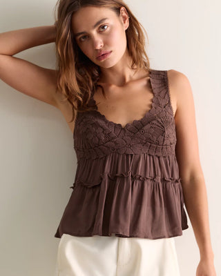 Woman wearing a brown lace top and white pants against a plain background