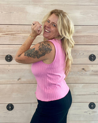 Woman in a pink sleeveless top posing against a wooden wall.