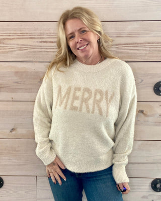 Woman wearing a cream sweater with 'MERRY' text against a wooden background
