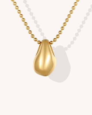 A gold teardrop pendant necklace with a smooth, polished finish on a gold ball chain, shown against a light off-white background with a soft shadow.