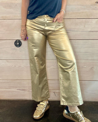 Woman wearing a blue t-shirt with a graphic design and gold pants against a wooden background