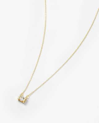 A delicate gold chain necklace with a small gold pendant featuring a clear gemstone, displayed on a clean white background.