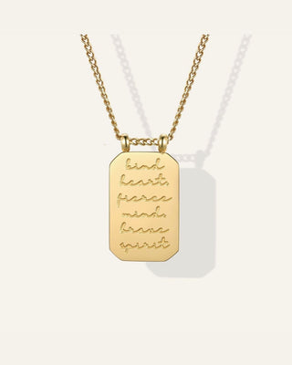A gold chain necklace with a rectangular dog tag pendant engraved with the words 'kind heart, fierce mind, sane spirit' in cursive, shown on a light cream background.