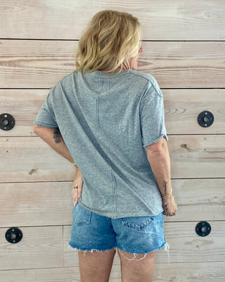 Person wearing a gray t-shirt and denim shorts standing against a wooden wall.