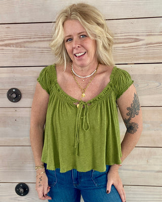Woman wearing a green top and blue jeans standing against a wooden background