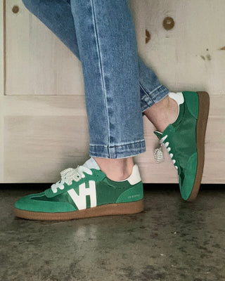 Green sneakers with white accents worn with blue jeans against a wooden background
