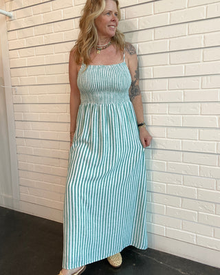 Woman wearing a blue and white striped dress standing against a light brick wall.