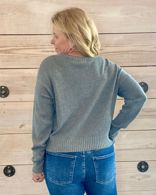 Person wearing a gray sweater and blue jeans standing against a wooden wall.