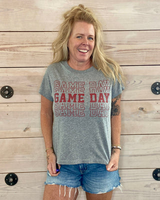 Person wearing a 'Game Day' t-shirt standing against a wooden wall.