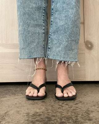 Person wearing light blue jeans and black sandals standing on a concrete floor.