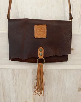 Brown leather handbag with tassel on a wooden surface