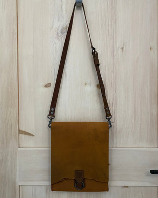 Brown leather bag with a strap on a light wooden floor