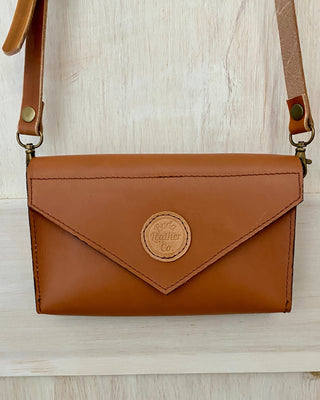 Brown leather crossbody bag with a visible brand logo on a light wooden surface.