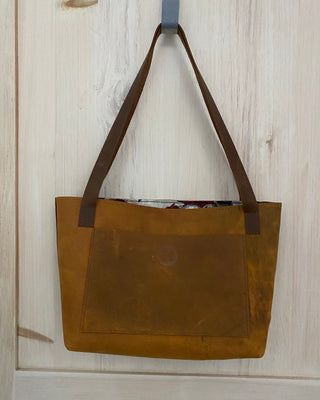 Brown leather tote bag on a light wooden surface
