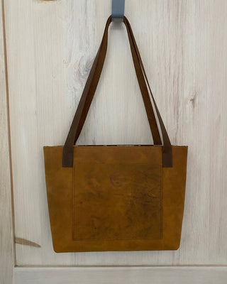 Brown leather bag with a strap on a light wooden floor