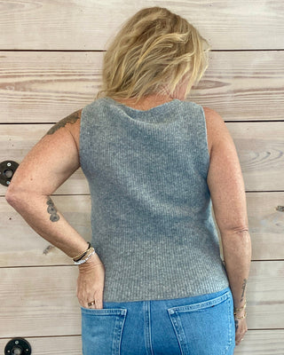 Person wearing a sleeveless gray top and blue jeans standing on a wooden deck.