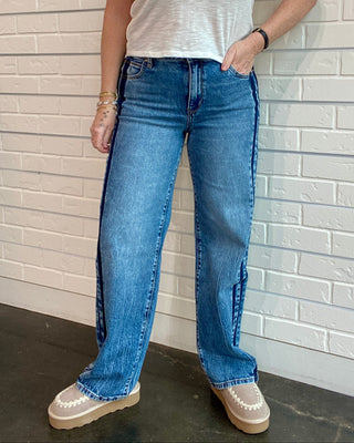 Person wearing a white t-shirt and blue jeans against a light brick wall.