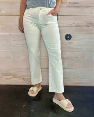 Person wearing a gray t-shirt, white pants, and sandals against a wooden wall.