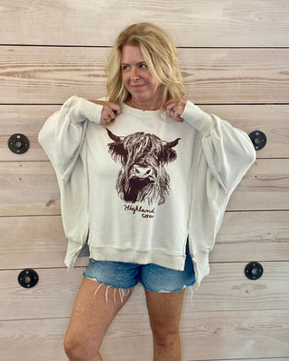 Woman wearing a white sweatshirt with a highland cow design against a wooden background