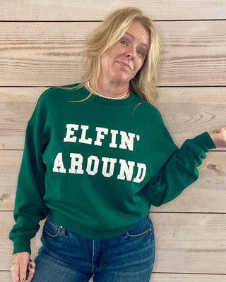 Person wearing a green sweatshirt with 'ELFIN' AROUND' text against a wooden background
