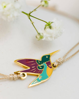 Colorful hummingbird-shaped pendant on a necklace with a white floral background