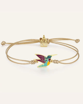 A gold-plated adjustable cord bracelet featuring a colorful enamel hummingbird charm and a small gold crown charm, displayed on a clean off-white background.
