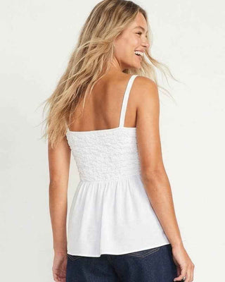 Woman wearing a white sleeveless top and dark shorts on a plain background