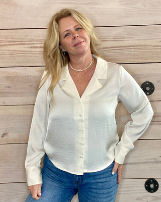 Woman wearing a white blouse and blue jeans standing against a wooden wall.