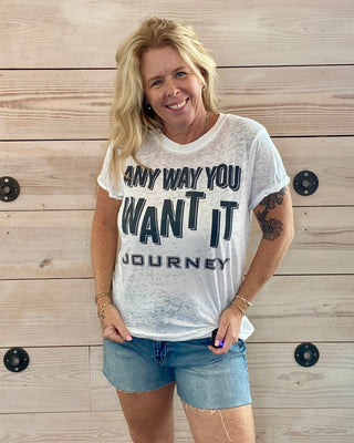 Woman wearing a white t-shirt with text standing against a wooden wall.