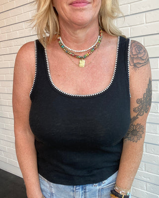 Person wearing a black tank top with white trim against a brick wall.