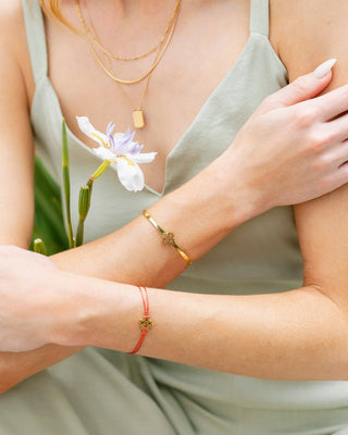 Close-up of a person wearing gold and red bracelets with a flower in the background