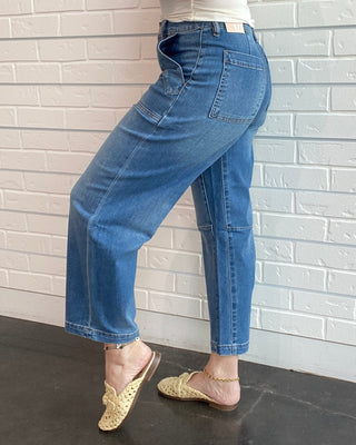 Person wearing blue jeans and a white top against a light brick wall.