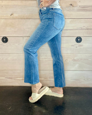 Person wearing blue jeans and a gray top against a wooden wall.