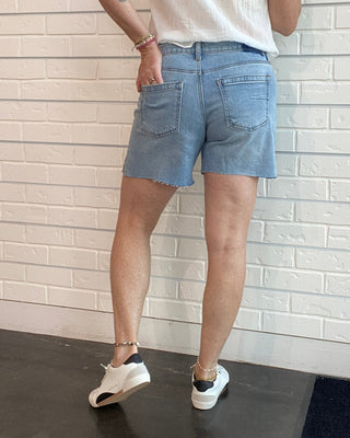 Person wearing a white sleeveless shirt and blue shorts standing against a white brick wall.