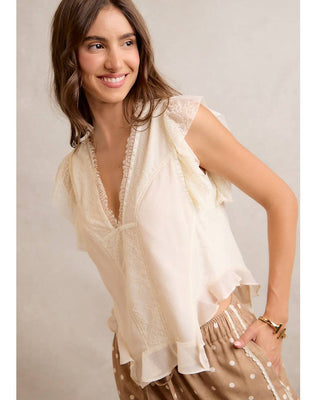 Woman wearing a light-colored blouse with lace details against a neutral background