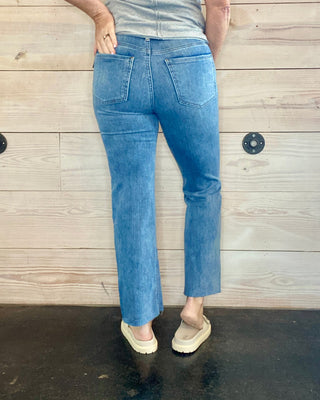 Person wearing a gray t-shirt and blue jeans standing against a wooden wall.