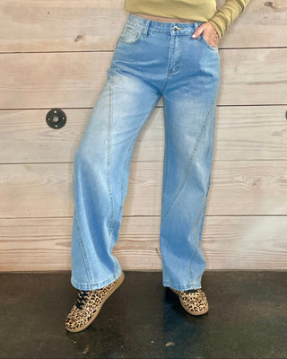Woman wearing a green long-sleeve shirt and blue jeans against a wooden background