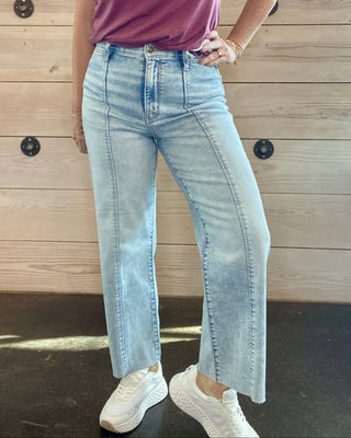 Person wearing a purple shirt and light blue jeans standing against a wooden wall.