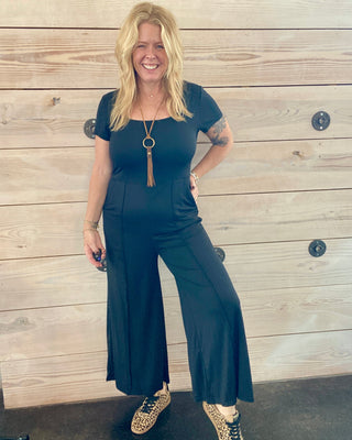 Woman in a black outfit standing against a wooden wall