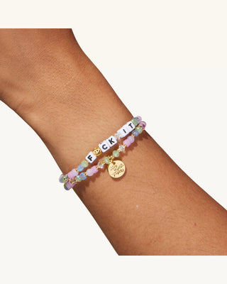 Multicolored beaded bracelet with a gold charm on a wrist against a white background