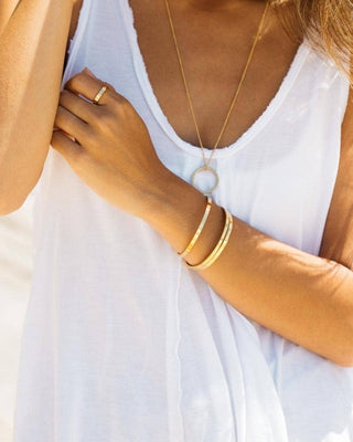 Close-up of a person wearing a white top and gold jewelry on a blurred background