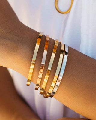 Gold bracelets on a wrist with a blurred white background