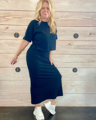 Woman wearing a black outfit with white sneakers against a wooden background