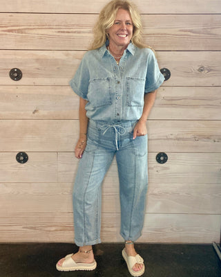 Woman wearing a denim outfit standing against a wooden wall.
