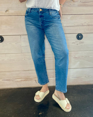 Person wearing a white t-shirt and blue jeans standing against a wooden wall.